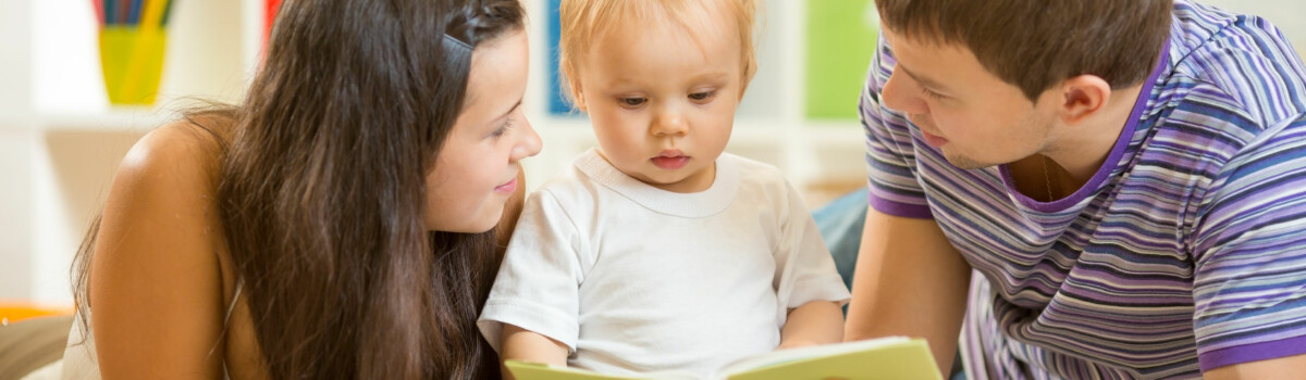 Young parents laid on the floor with baby reading