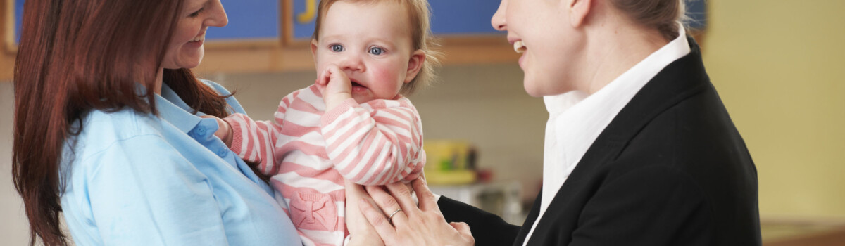 Nursery worker holding child, while talking to parent about their data protection practices