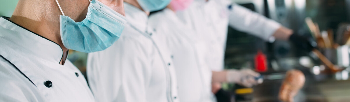 Hospitality chefs in protective face masks cooking food during COVID-19 outbreak